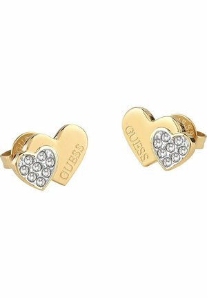 Orecchini a perno a forma di cuore in tonalità oro, con un lato decorato da strass trasparenti e l'altro inciso con la scritta "GUESS". Finitura liscia e superficie lucidata.