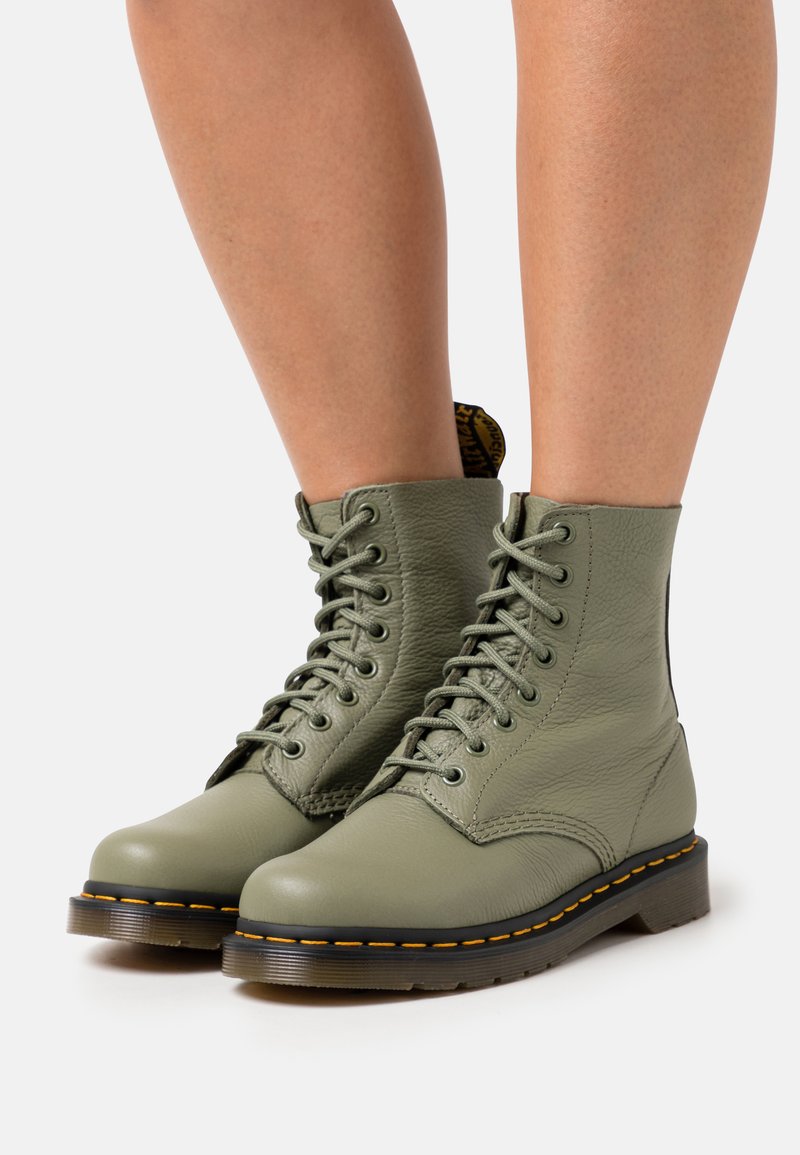 Bottines en cuir olive avec un design à lacets, bout rond et surpiqûres jaunes le long de la semelle en caoutchouc ; finition en cuir texturé.