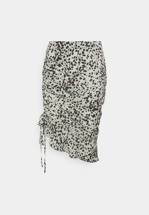 Biała spódnica z czarnym nieregularnym wzorem w cętki, marszczonym fasonem, wiązaniami po bokach i asymetrycznym dołem.