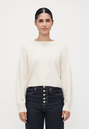 Cremfarbener, kurz geschnittener Pullover mit langen Ärmeln, geripptem Saum und rundem Halsausschnitt, kombiniert mit hochgeschnittenen, dunkelblauen Jeans aus Denim mit silbernen Knöpfen.