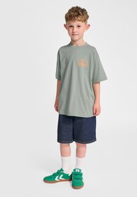 Ljusgrön oversized t-shirt med orange grafik, mörka jeansshorts, vita strumpor och gröna sneakers med vita detaljer.