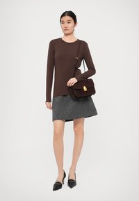 Ruskea pitkähihainen toppi, harmaa tweed-hame, mustat korkokengät ja tumma ruskea mokkahandbag, jossa on kultainen solkiyksityiskohta.