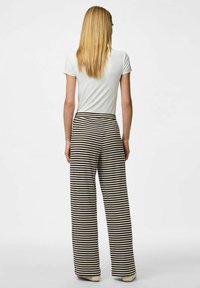 Un pantalon large présente un motif rayé noir et crème, fabriqué à partir d'un tissu doux et texturé. Associé à un haut blanc ajusté.