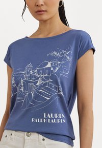 Mėlynas trumpomis rankovėmis marškinėliai su baltu kontūru vaizduojančiu kraštovaizdį ir užrašu "LAUREN RALPH LAUREN" apačioje.