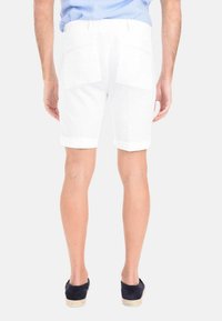 Pantaloni corti bianchi in lino con orli risvoltati, dotati di due tasche posteriori. Indossati con una camicia blu e scarpe blu navy, mostrano uno stile casual.
