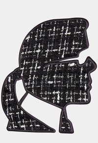 Parche texturizado en blanco y negro con la forma de un perfil con coleta, que presenta un patrón tejido y está contorneado en tela negra.
