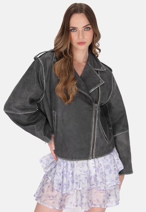 Veste de moto en cuir gris avec une coupe légèrement oversize, fermeture éclair devant et détails de couture contrastants, associée à une jupe florale superposée.
