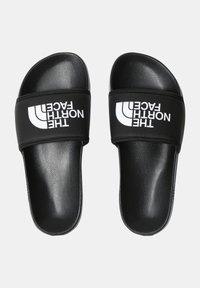 Black slide sandals with a textured strap featuring a white logo. Smooth, glossy footbeds, open toe and heel design.