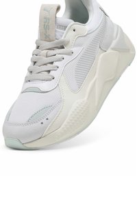 Bílé a světle šedé sportovní tenisky s texturovanou síťovinou a koženými panely, silnou podrážkou a šedými tkaničkami, nakloněné pro přední a boční pohled.