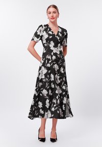 Swarte blomstret kjole med innpakningsdesign, korte ermer og en flytende A-linje skjørt. Har hvite blomster mønstre og et lett stoff.