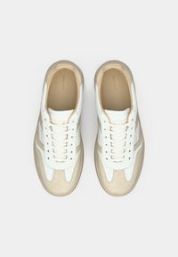 Λευκά και μπεζ αθλητικά παπούτσια με ανώτερο μέρος από δέρμα και σουέτ, στρογγυλή μύτη, σχέδιο με κορδόνια και χρυσό λογότυπο στη γλώσσα.
