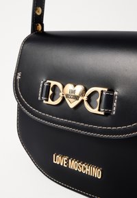 Black leather handbag with gold heart-shaped hardware, "LOVE MOSCHINO" branding, and contrasting stitching details. Adjustable strap included.