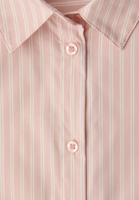 Světle růžová halenka s bílými vertikálními pruhy, špičatým límečkem a ladícími knoflíky vpředu. Hladká texturovaná tkanina.