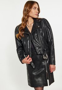 Giacca da moto in pelle nera con finitura testurizzata, chiusura con zip e dettaglio con cintura. La giacca presenta spalle imbottite e accessori in argento.