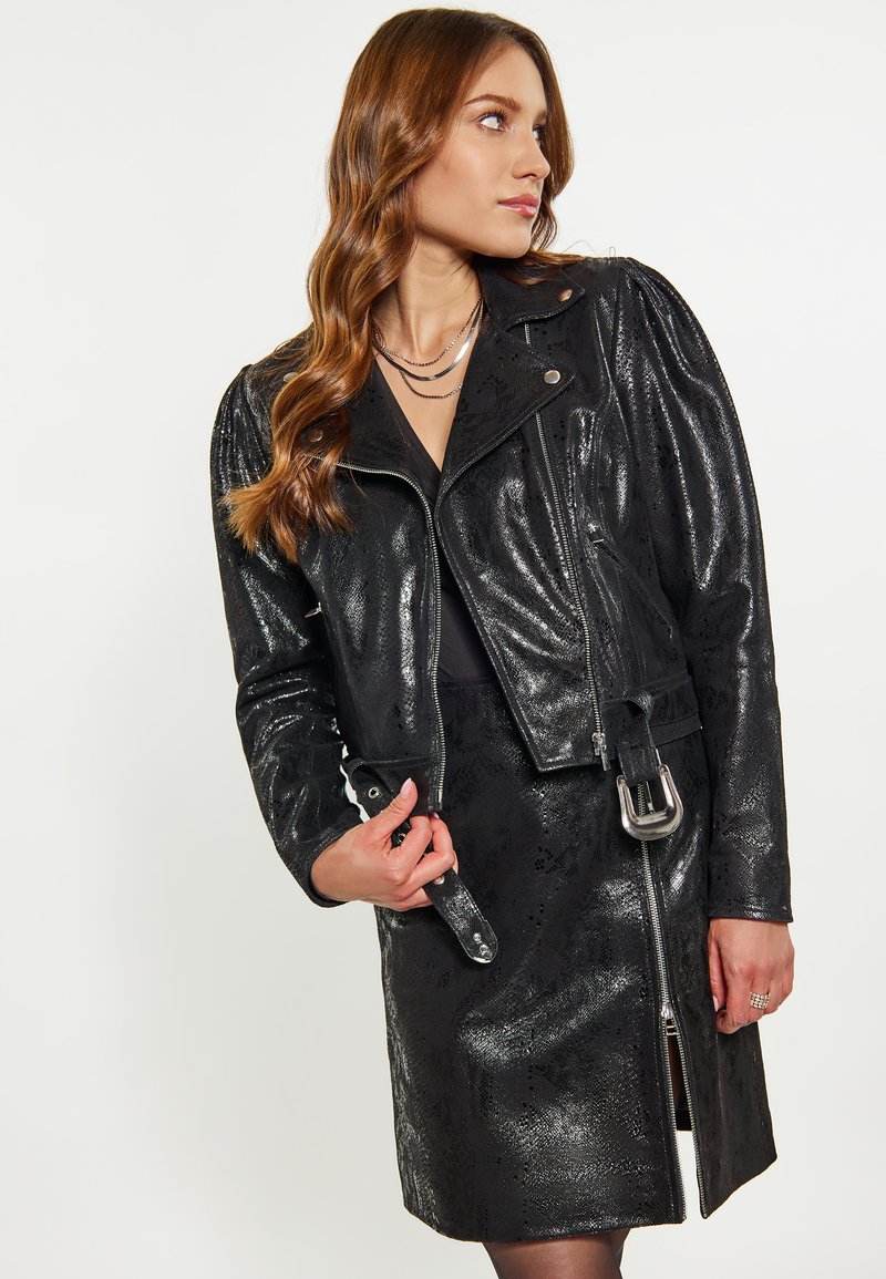 Giacca da moto in pelle nera con finitura testurizzata, chiusura con zip e dettaglio con cintura. La giacca presenta spalle imbottite e accessori in argento.