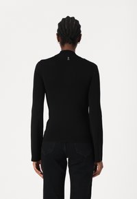 Haut noir à manches longues au design ajusté et à texture côtelée, avec un petit logo brodé sur le col au dos.