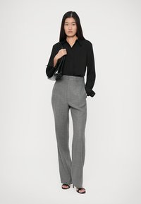 Cămașă neagră cu mâneci lungi, purtată cu pantaloni gri cu talie înaltă. Costumul prezintă o textură fină și este completat de o geantă neagră.
