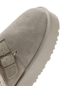 Calzature in suede grigio con suola in gomma piatta. Presentano un dettaglio con fibbia laterale, una superficie liscia e un design a punta rotonda.