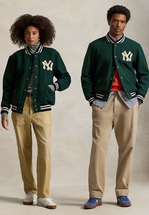 Vihreät villakankaasta valmistetut yliopistolaukkupojat vaaleanbeigeillä yksityiskohdilla, yhdistettynä khaki-housuihin. Mallit käyttävät teksturoituja pyöreäkauluksisia paitoja ja neutraalivärisiä lenkkikenkiä.
