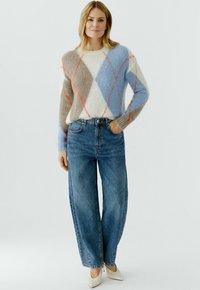 Trui van meerkleurige pluizige garen met ruitpatroon in wit, blauw en bruin; gecombineerd met hoge taille wijde blauwe jeans en lichte schoenen.