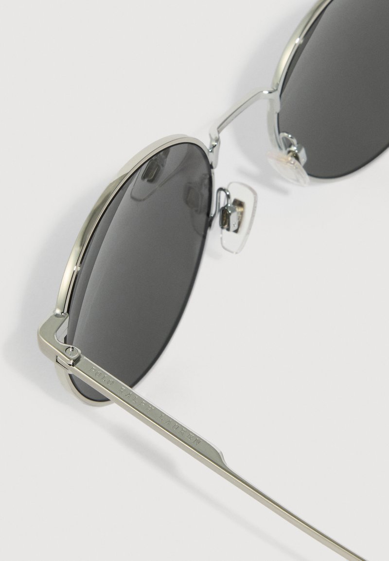 Round sunglasses featuring black lenses, silver metal frames, adjustable nose pads, and engraved logo detail on the temple.
