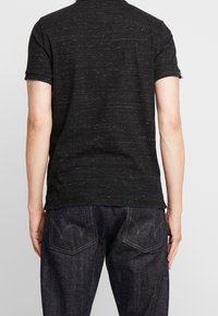 Polo shirt noir à manches courtes avec une finition texturée. Doté d'un col classique et de poignets roulés, associé à un jean bleu foncé mettant en valeur les poches arrière.