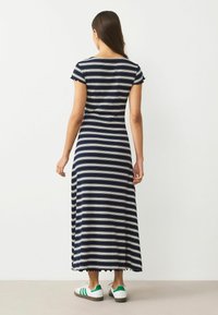 Námořnická modrá a bílá pruhovaná maxi šaty s krátkými rukávy, zvlněným lemem a přiléhavým korzetem. Kombinováno s bílými teniskami s zelenými pruhy.