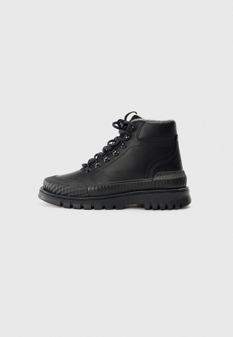 Botte montante noire avec semelle épaisse crantée, fermeture à lacets avec œillets métalliques et col rembourré à la cheville, présentée sur un fond clair uni.