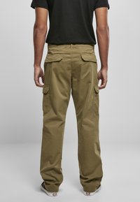 Pantalons cargo couleur kaki avec une coupe décontractée, dotés de poches latérales et d'une texture lisse. Portés avec un T-shirt noir et des baskets.