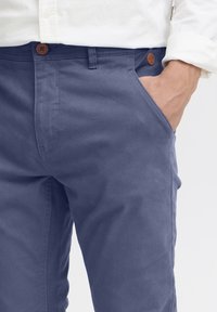 Chinos en coton navy avec une poche frontale, fermeture à bouton marron et un tissu texturé au design slim.
