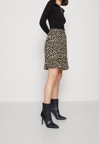 Svart långärmad topp matchad med en knälång kjol i svart och beige med prickar, prydd med en volangkant, kompletterad med svarta klackiga ankelstövlar.