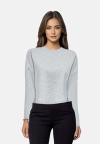 Felpa grigia chiaro a maniche lunghe con colletto rotondo, caratterizzata da una vestibilità rilassata e una texture morbida. Indossata con pantaloni scuri.