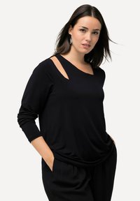 Schwarzes Langarmoberteil mit rundem Halsausschnitt und Ausschnitt an der Schulter. Weicher Stoff mit lockerer Passform, ausgestattet mit seitlichen Taschen.