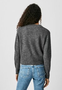 Gray knit sweater with a round neck and long sleeves, paired with light blue denim jeans featuring back pockets. Soft texture, relaxed fit.
