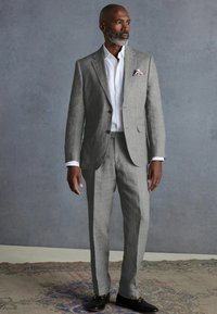 Grau Leinenanzug mit tailliertem Schnitt, weißem Hemd und gemustertem Taschentuch. Schwarze Slipper runden das Ensemble ab. Einfaches und elegantes Design.