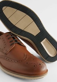 Chaussures habillées en cuir brun avec un design perforé et des détails en brogue. Semelle en caoutchouc avec un motif texturé noir et beige pour une meilleure adhérence.
