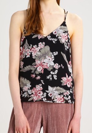 Kvinde iført en sort blomster spaghetti strop top med pink og grå blomster og løse pink teksturerede bukser.