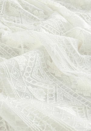 Tessuto in pizzo bianco, con motivi intricati e accenti testurizzati, dalla qualità morbida e delicata e drappeggiato a strati.