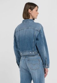 Ljust blå denimjacka med en kortad passform, klassisk krage och tryckknappdetaljer. Har avslappnad passform och design med söm över ryggen.