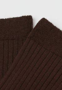 Calcetines marrones con diseño de punto texturizado, que cuentan con un borde enrollado en la parte superior y finas líneas verticales para un detalle adicional.