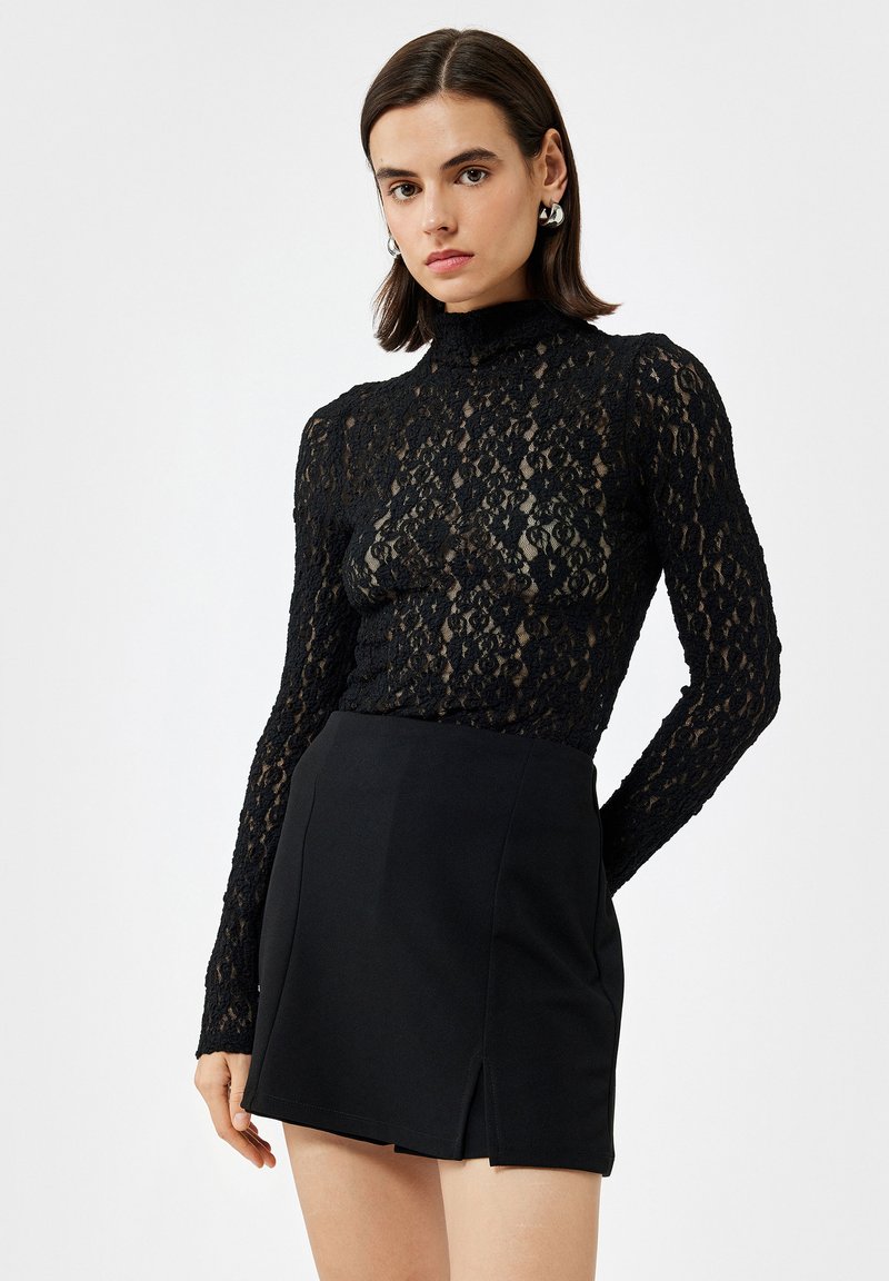 Zwarte kanten longsleeve-top met hoge hals en ingewikkeld bloemmotief, gecombineerd met een aansluitende zwarte minirok met een split aan de voorkant.