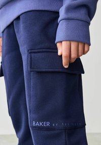 Tumedate sinised cargo dressipüksid, külgtasku, soonikuga sääred ja trükitud logo alläärtes. Pehme tekstuur ja mugav lõige.