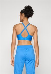 Blå sportsbh med racerback-design, med kryssede stropper og Under Armour-merke. Kombinert med matchende blå treningsbukser.