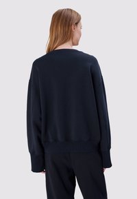 Marineblauwe oversized sweatshirt met geribbelde textuur, verzonken schouders en brede manchetten; cropped lengte. Minimalistisch ontwerp, zonder zichtbare logo's.