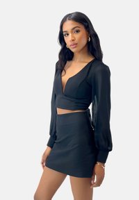 Sort langærmet cropped top med dyb V-udskæring og matchende mini nederdel. Begge dele har en glat tekstur og tætsiddende design.
