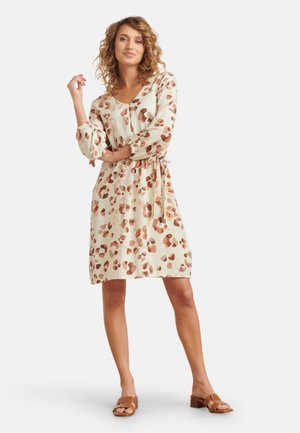 Short-sleeve, knee-length dress in a light cream fabric with brown and peach abstract spots, featuring a tie waist and elastic cuffs.