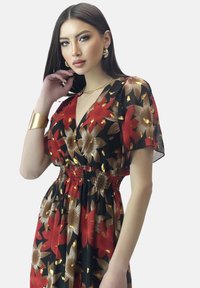 Vestido floral rojo y negro con acentos dorados, que presenta un profundo escote en V, mangas cortas de volantes y detalle de cintura fruncida.