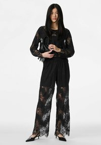 Czarny koronkowy strój składający się z długiego rękawa i spodni o szerokich nogawkach. Przezroczysta tkanina z kwiatowymi wzorami; w połączeniu z czarnymi szpilkami z ostrym noskiem.