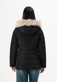 Giubbotto imbottito nero con cappuccio foderato in pelliccia leggera. Il design presenta sezioni trapuntate e maniche lunghe, abbinato a jeans in denim.