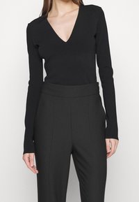 Svart långärmad topp med v-ringning tillsammans med svart högmidjad byxa. Tyget ser mjukt ut och passformen är skräddarsydd efter kroppens form.
